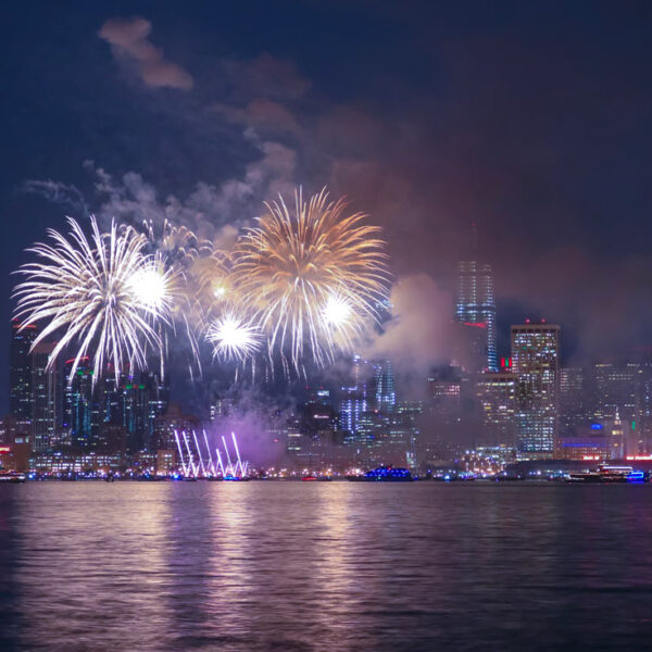 Des feux d’artifice explosent au-dessus de New York avec leurs reflets dansant au-dessus de l’eau.