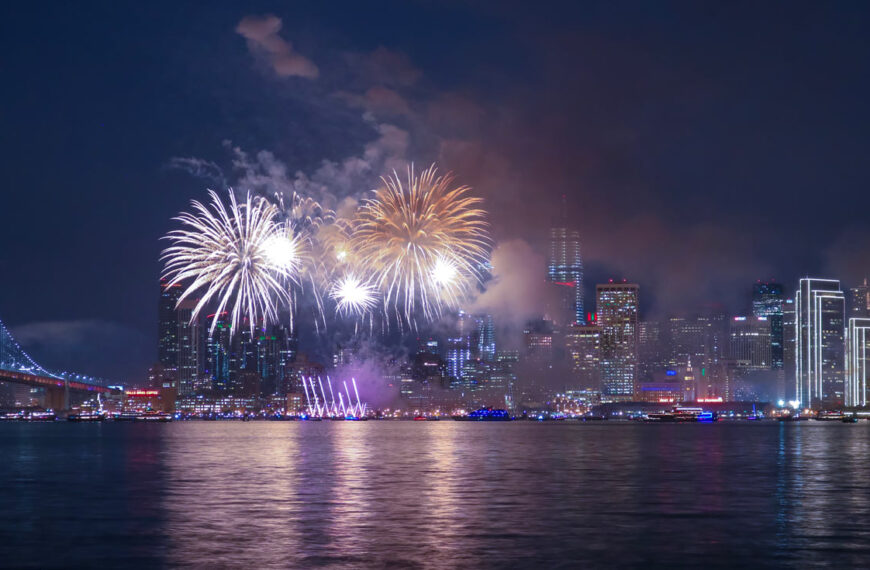 Des feux d’artifice explosent au-dessus de New York avec leurs reflets dansant au-dessus de l’eau.