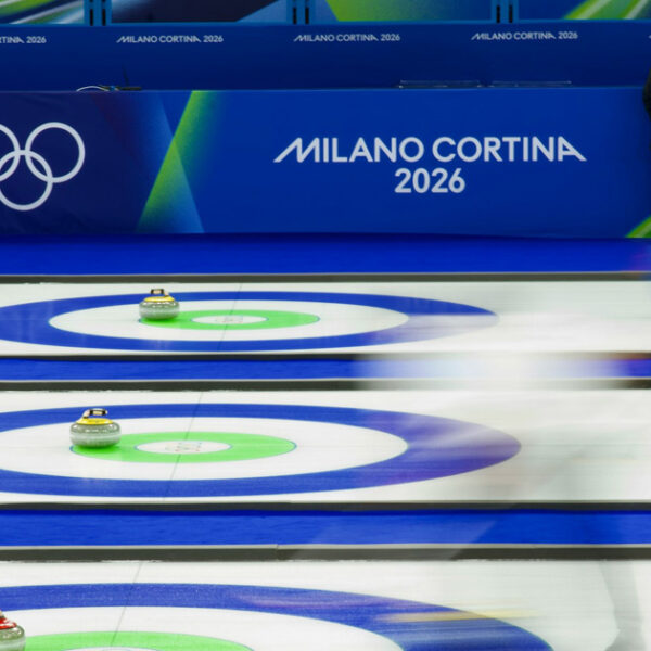 Un joueur de curling se prépare à lancer une pierre aux Jeux olympiques de Milano Cortano et un silence prononcé et une concentration s’installent sur la patinoire.